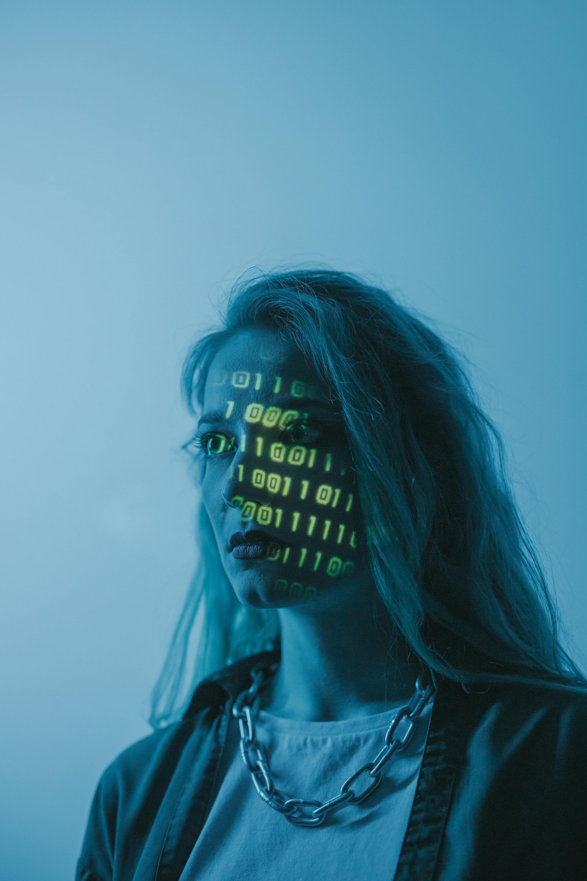 Binary code is projected onto a person’s face, creating a technological aesthetic against a blue-toned background.