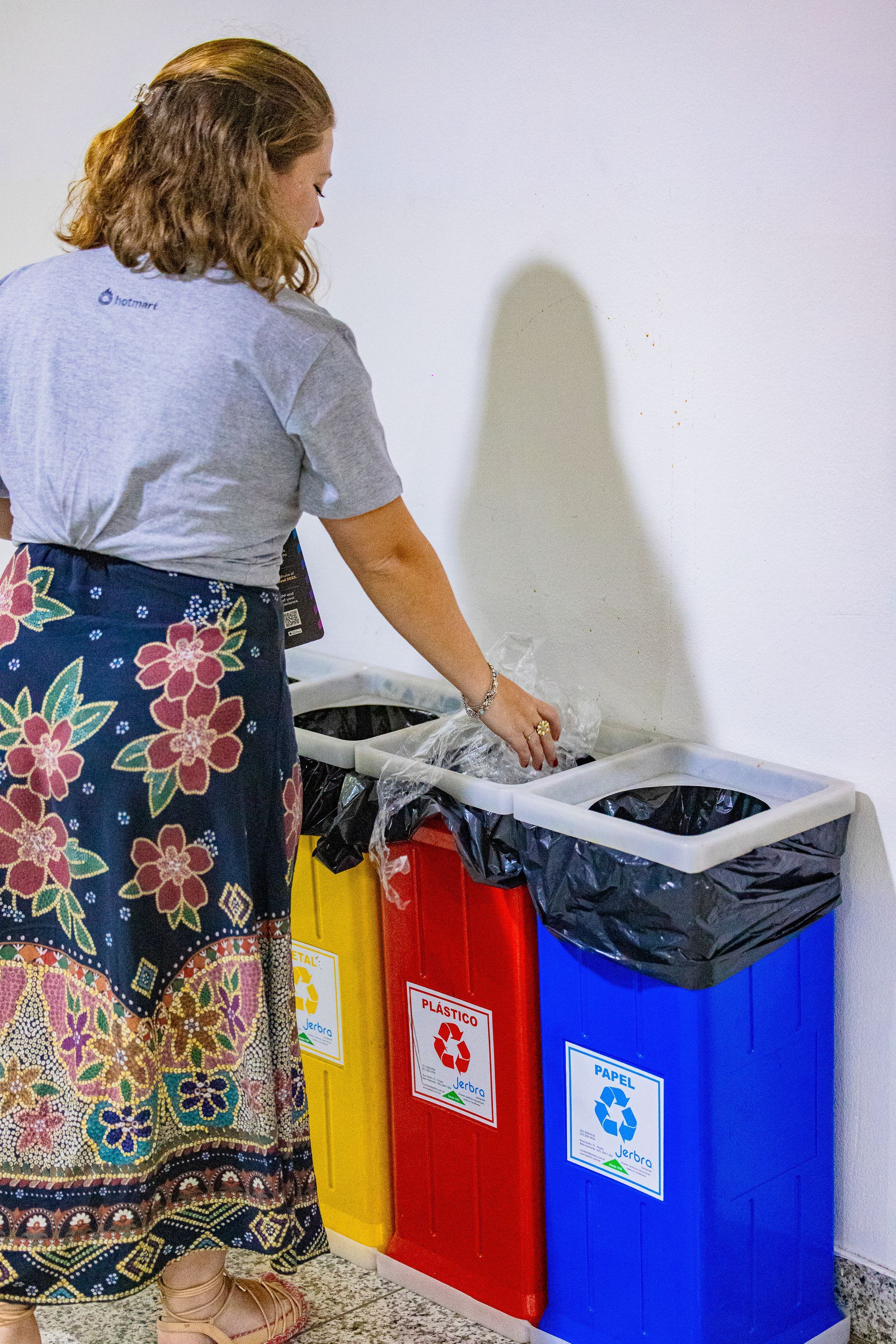 Uma mulher está colocando lixo em uma lixeira de reciclagem.