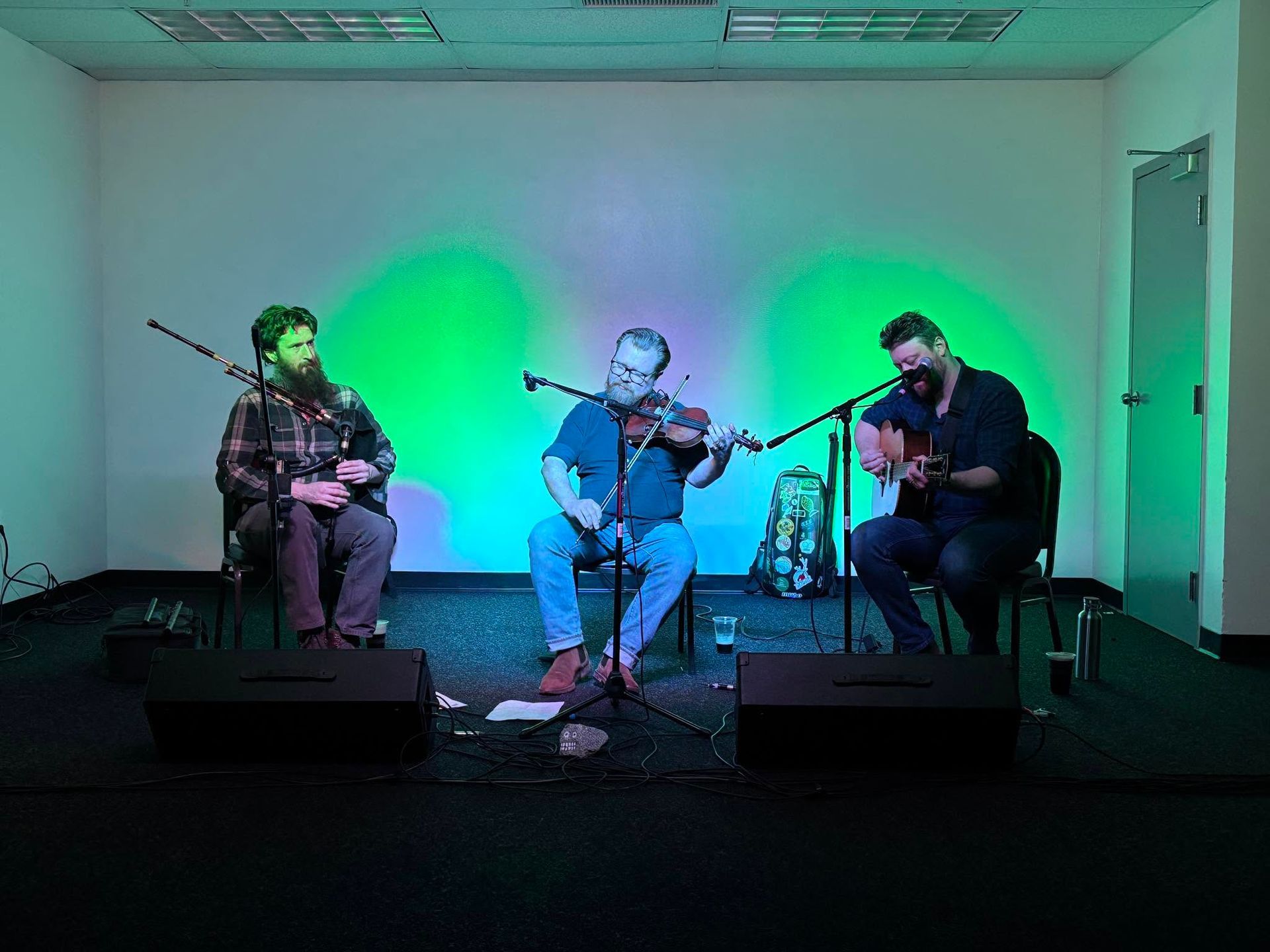 Three musicians performing on stage under green and blue lights in a small venue