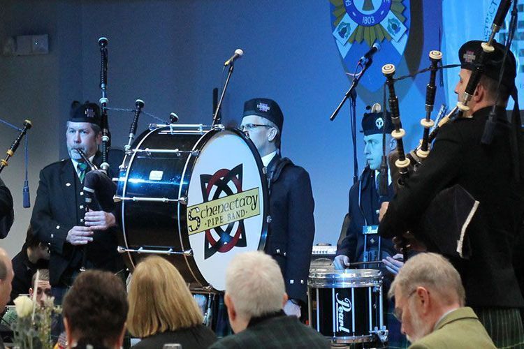 Bagpipers and a drum player perform on a stage in front of an audience.
