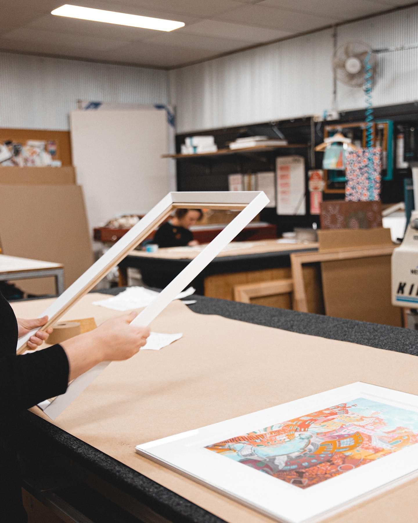 A Person Is Holding a Picture Frame Over a Painting on A Table — B Framed Picture Framing in Ballina, NSW