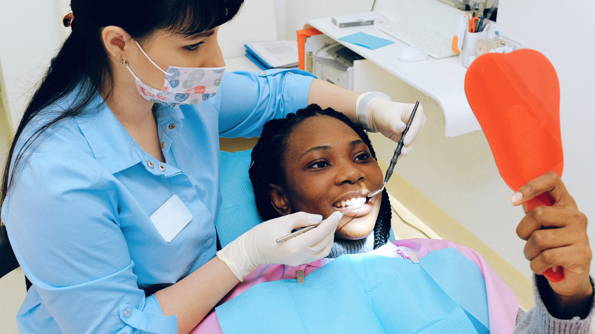 Woman wearing a bright yellow shirt sitting in a dental chair, smiling with mouth open towards a dentist. 
