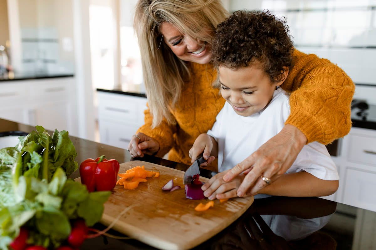 A grandma cuts vegetables with her grandson.