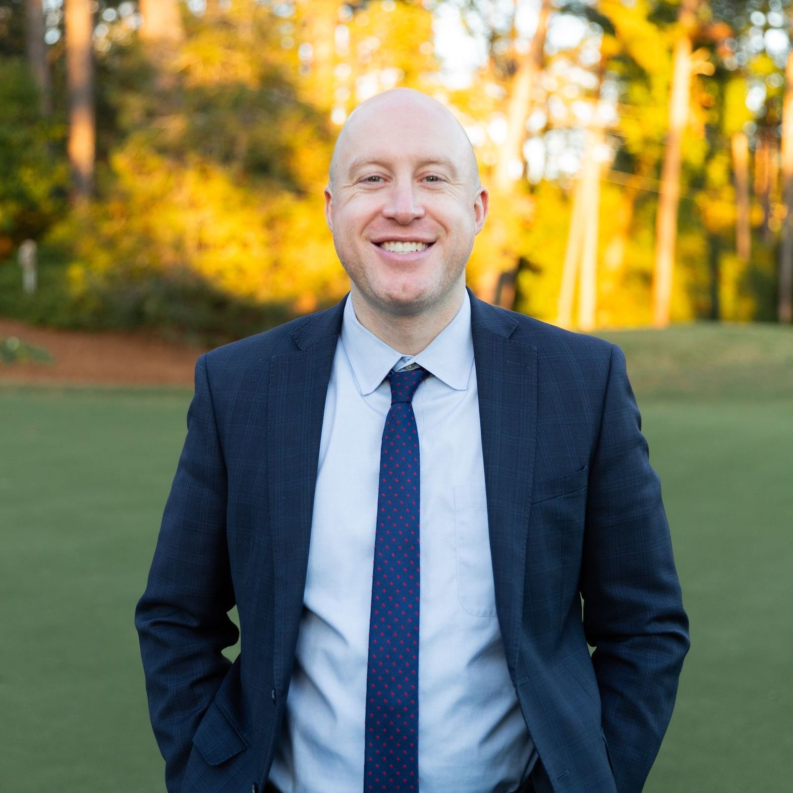 A man in a suit and tie is smiling with his hands in his pockets.