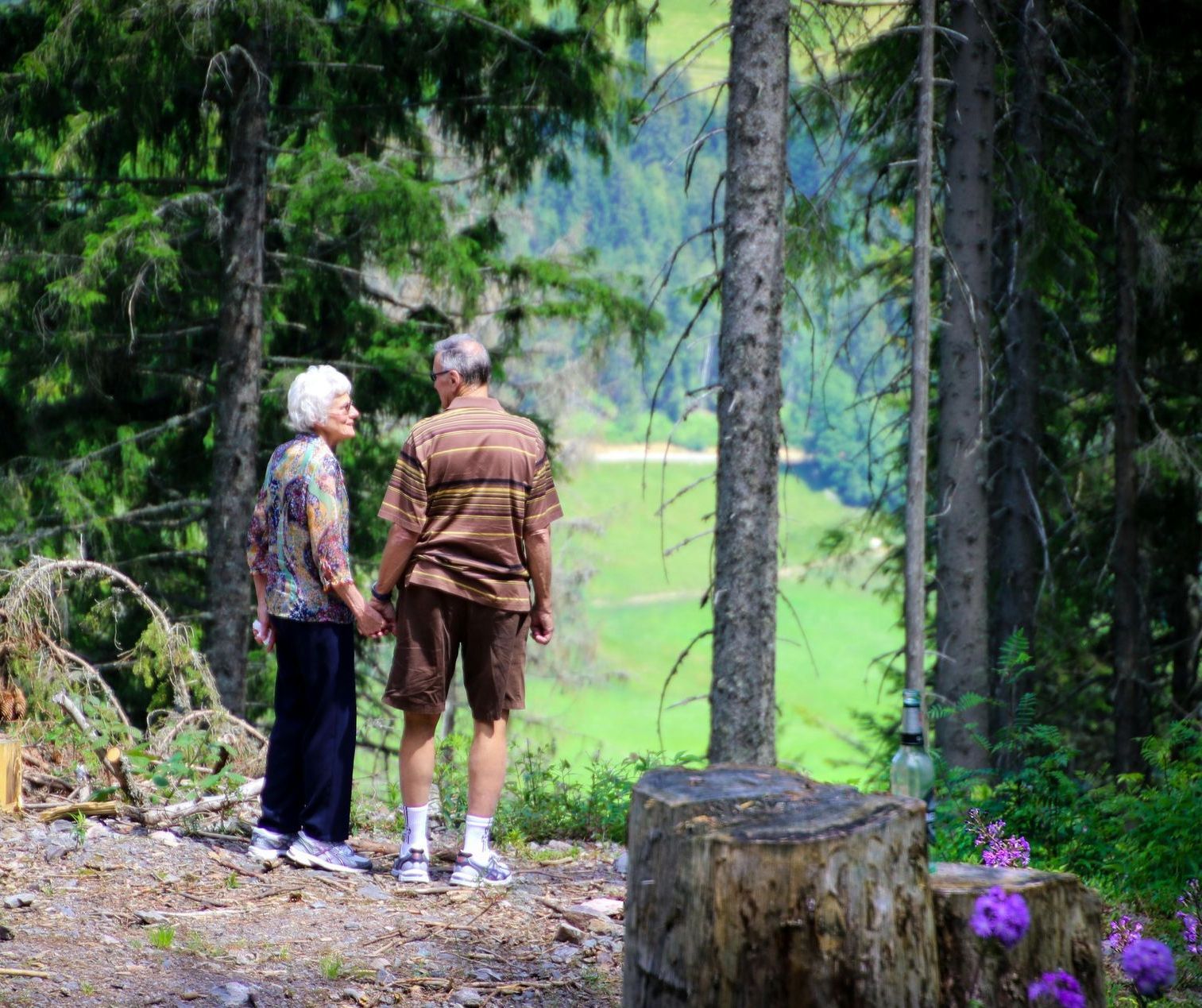 A man and a woman are standing in the woods holding hands