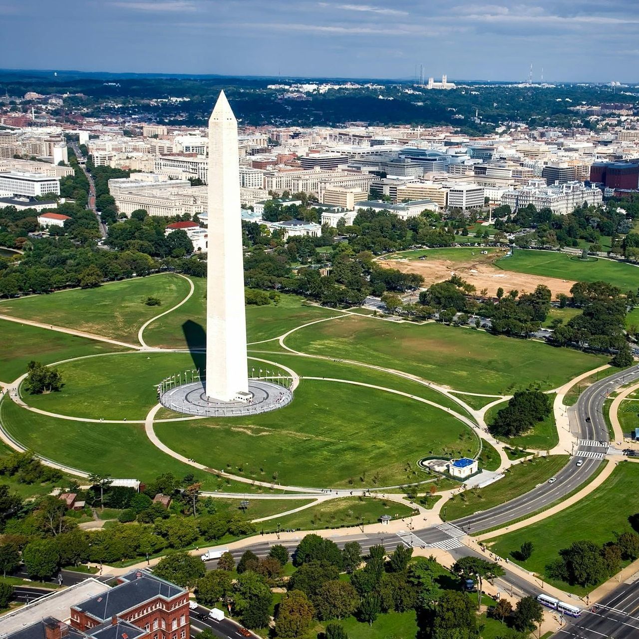Washington Monument stands tall in Washington, D.C., with green fields and city buildings in the background.