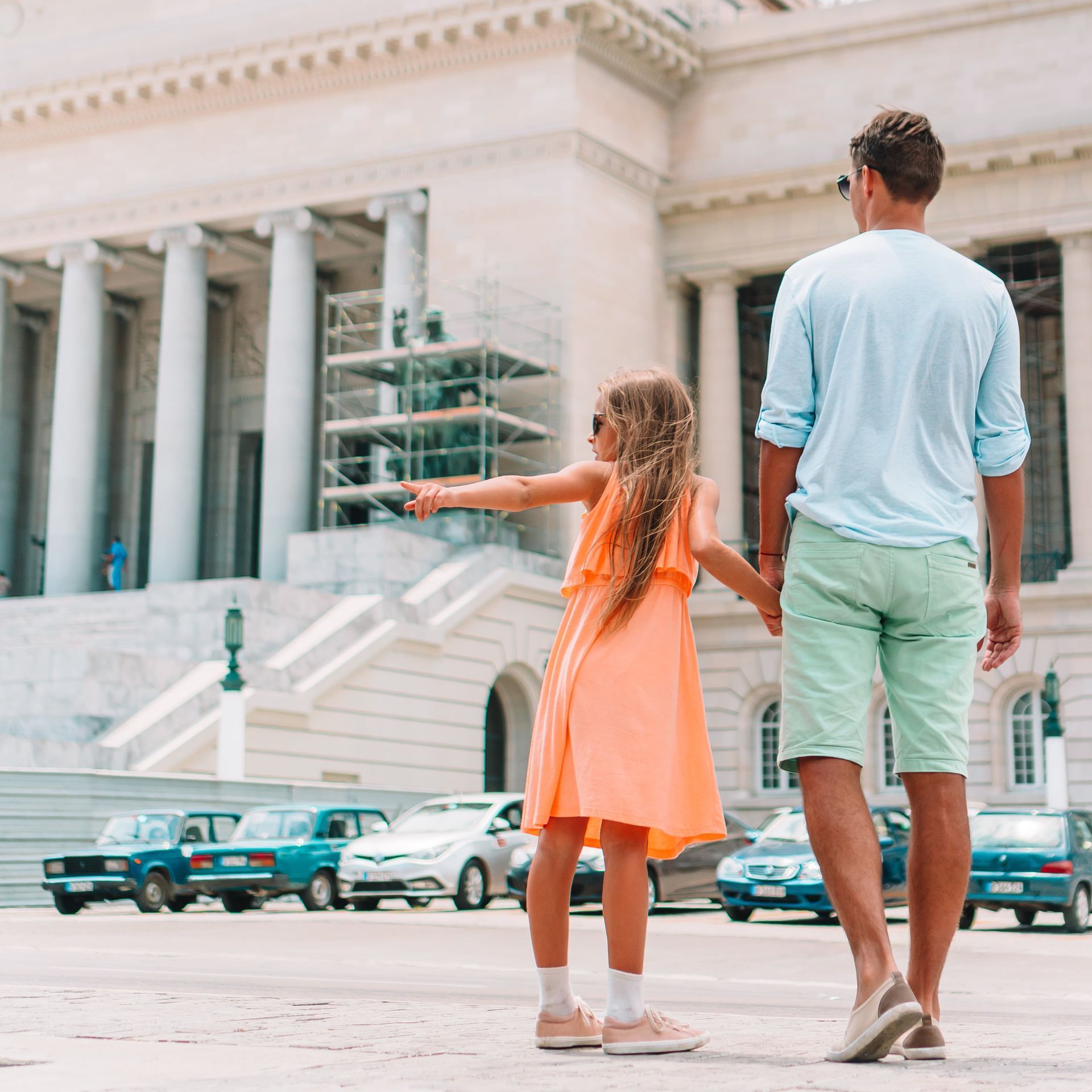 A man and a little girl are holding hands in front of a building