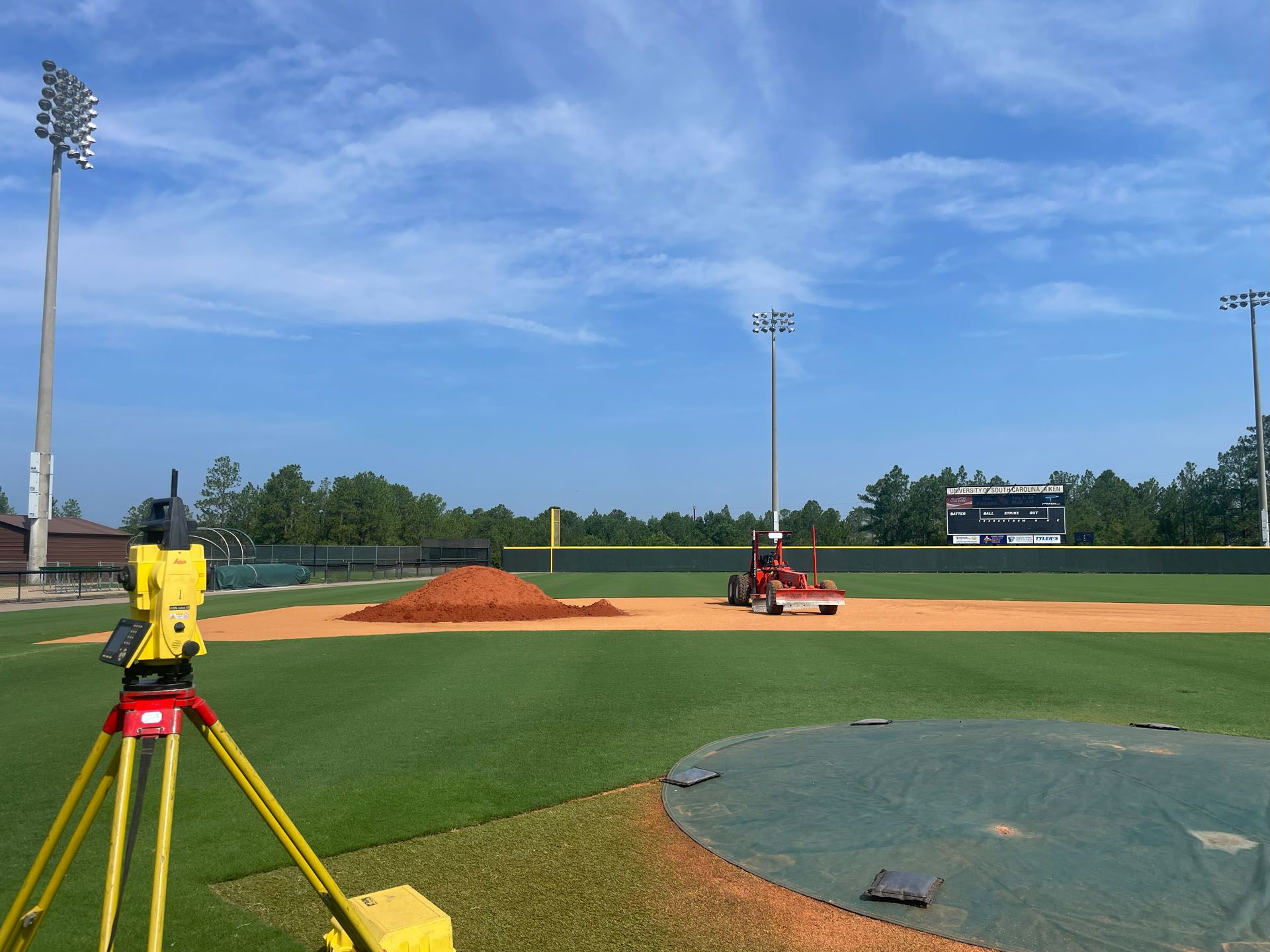 Baseball field under construction with surveying equipment and machinery; blue sky.
