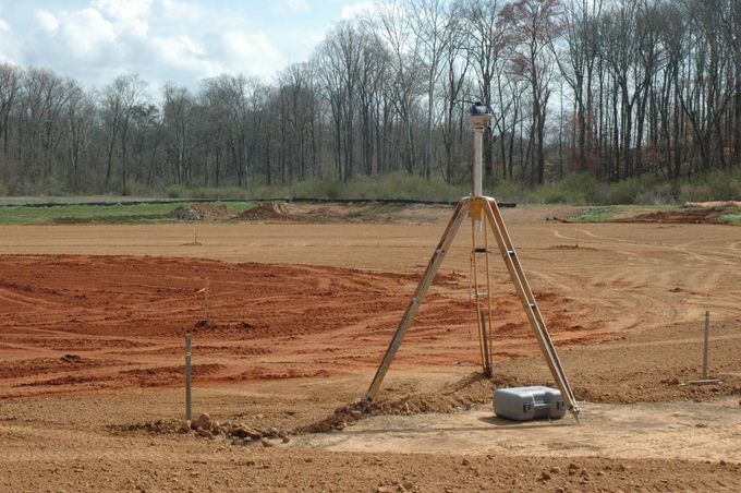 Surveying equipment set up in a dirt field with a backdrop of trees.