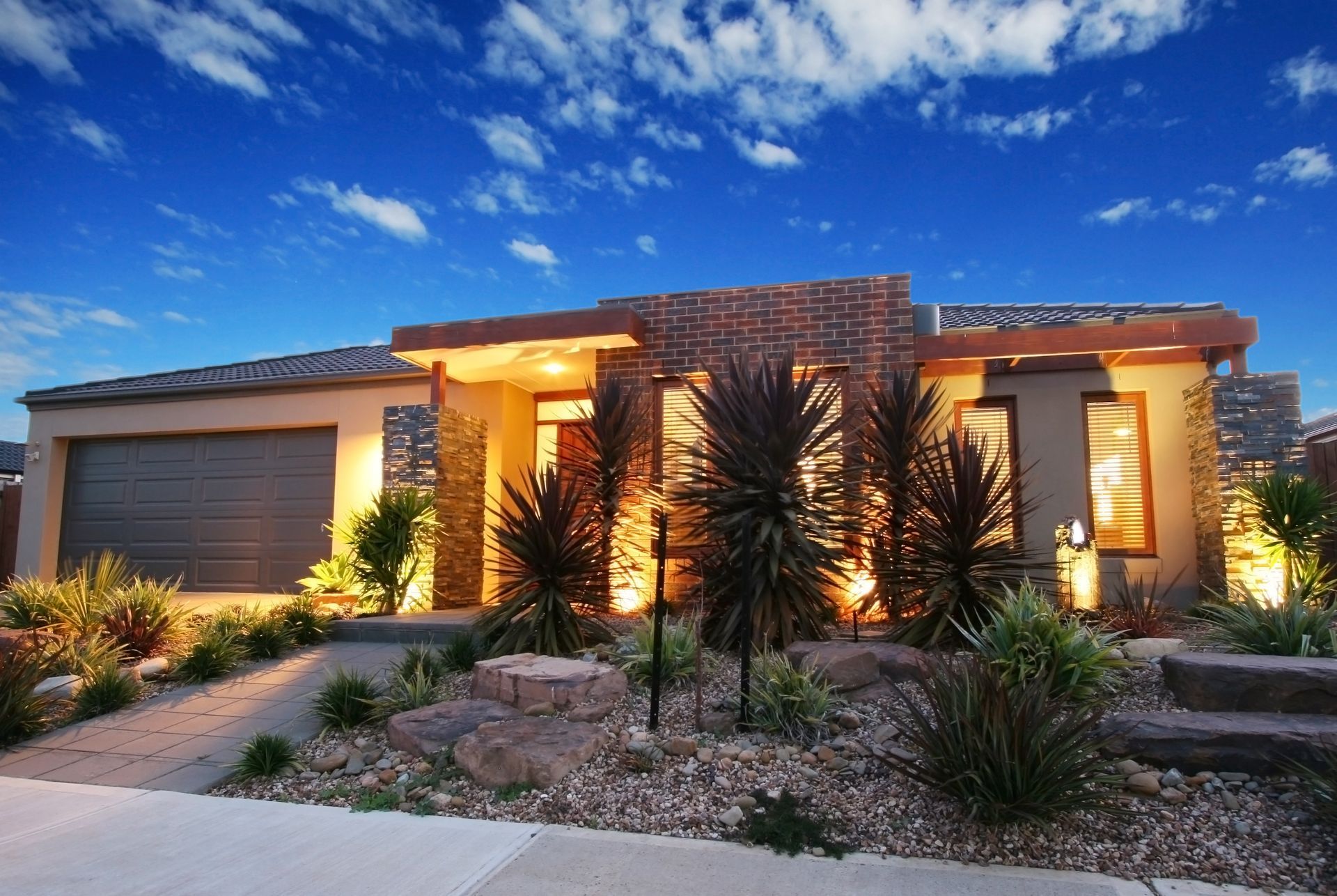 Modern home exterior with stone accents, landscaped yard, and blue sky.