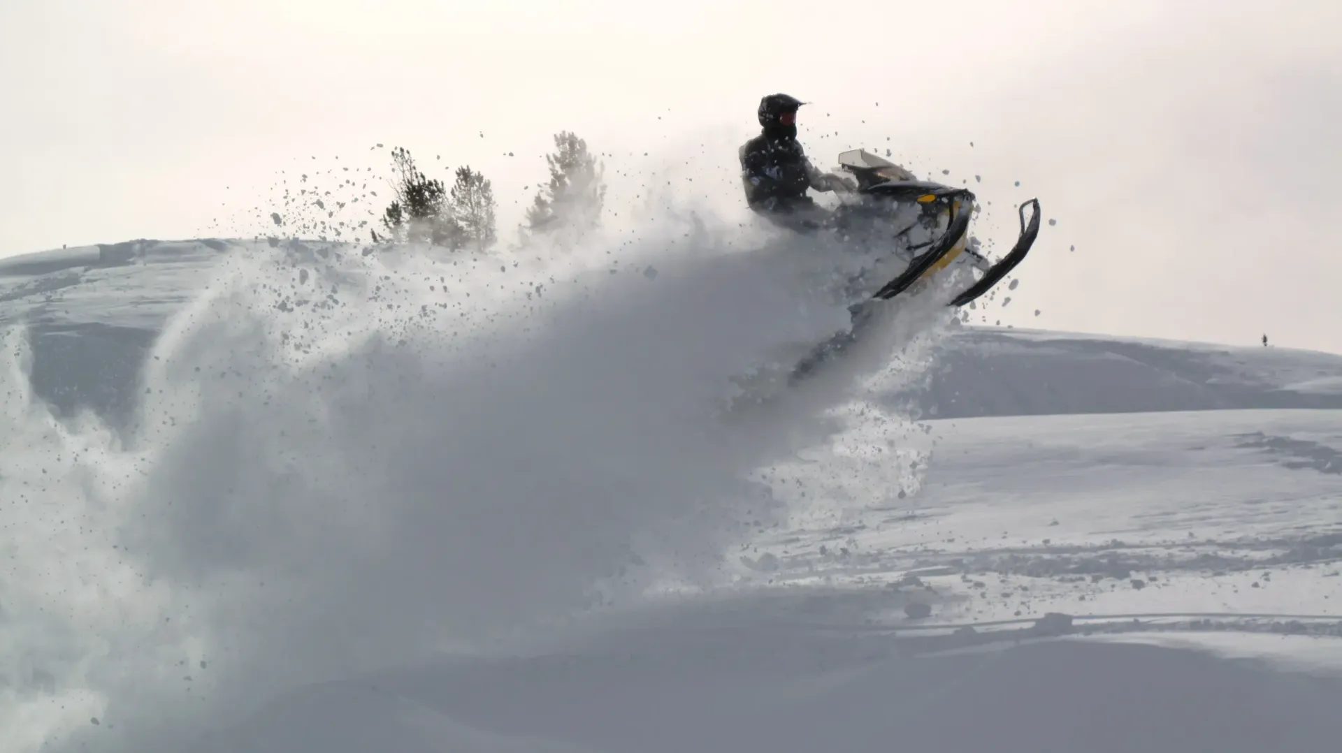 Snowmobile launching through deep snow, spraying a white plume against a bright winter landscape