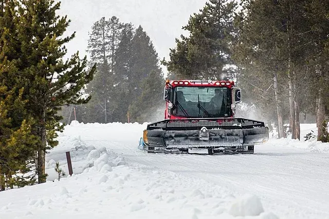 Red snow groomer clearing a snowy forest trail in winter