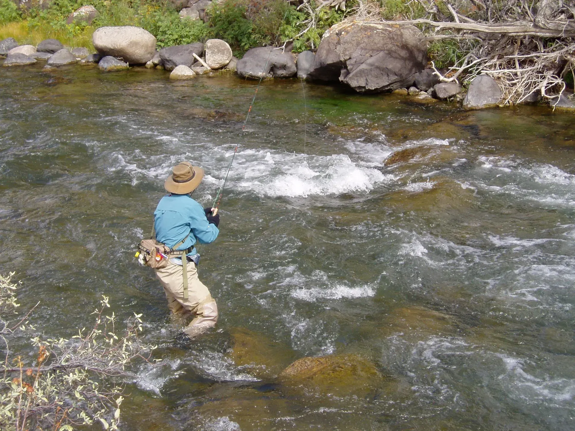 Person fishing in a shallow river near the rocky bank