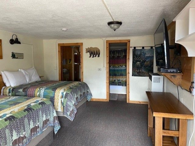 Hotel room with two beds, desk, TV, and open closet in a beige interior.