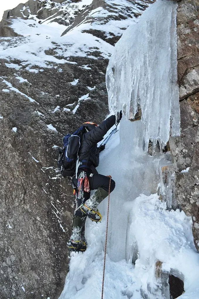 Ice climber scaling a frozen waterfall with ropes and climbing gear