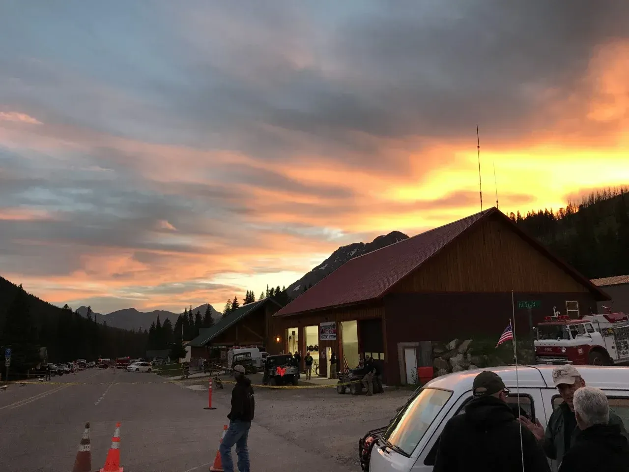Sunset over a lodge parking lot with people and cars outside a red-roofed building