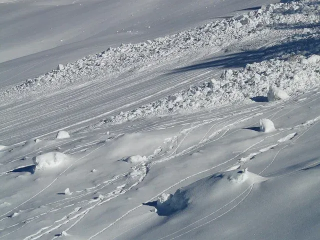 Wind-swept snowdrifts on a snowy mountainside under gray sky