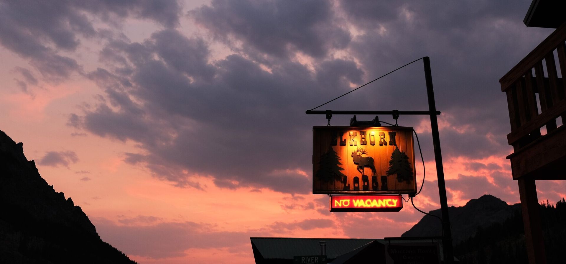 Pink sunset sky over a street with a lit hanging sign and dark building silhouettes