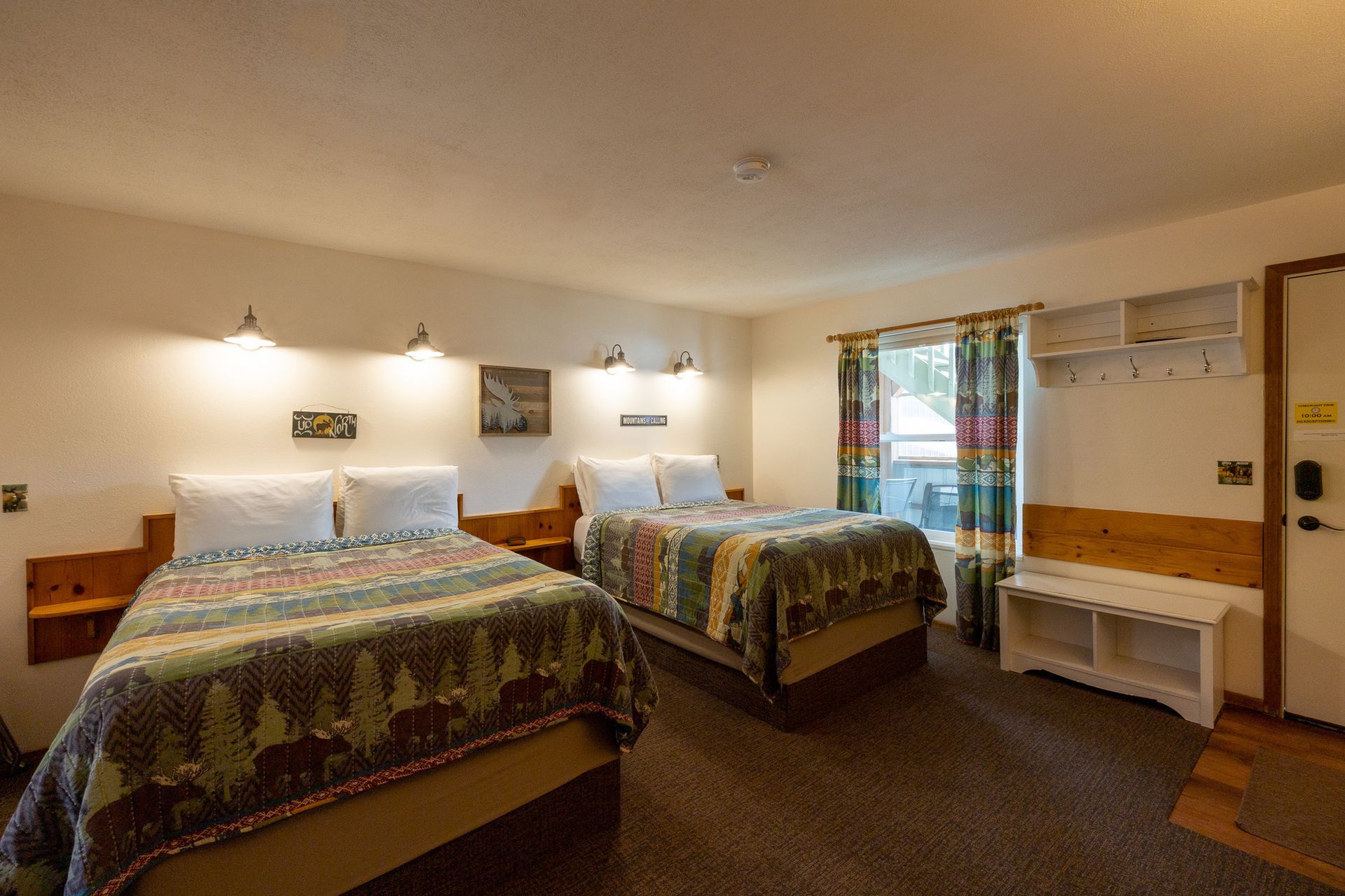 Hotel room with two beds, wall lamps, a window, and a small desk area