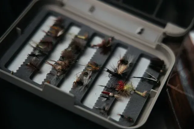 Open fly box with several fishing flies and lures arranged in foam slots