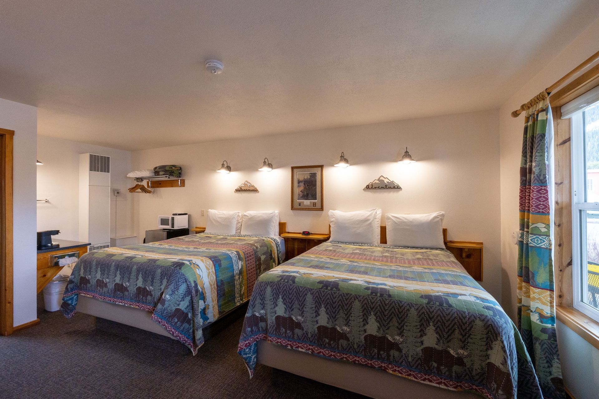 Hotel room with two beds, colorful quilts, wall lamps, and a window with blinds