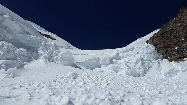 Snowy mountain glacier under a clear blue sky, with rocky slopes framing the icy valley.