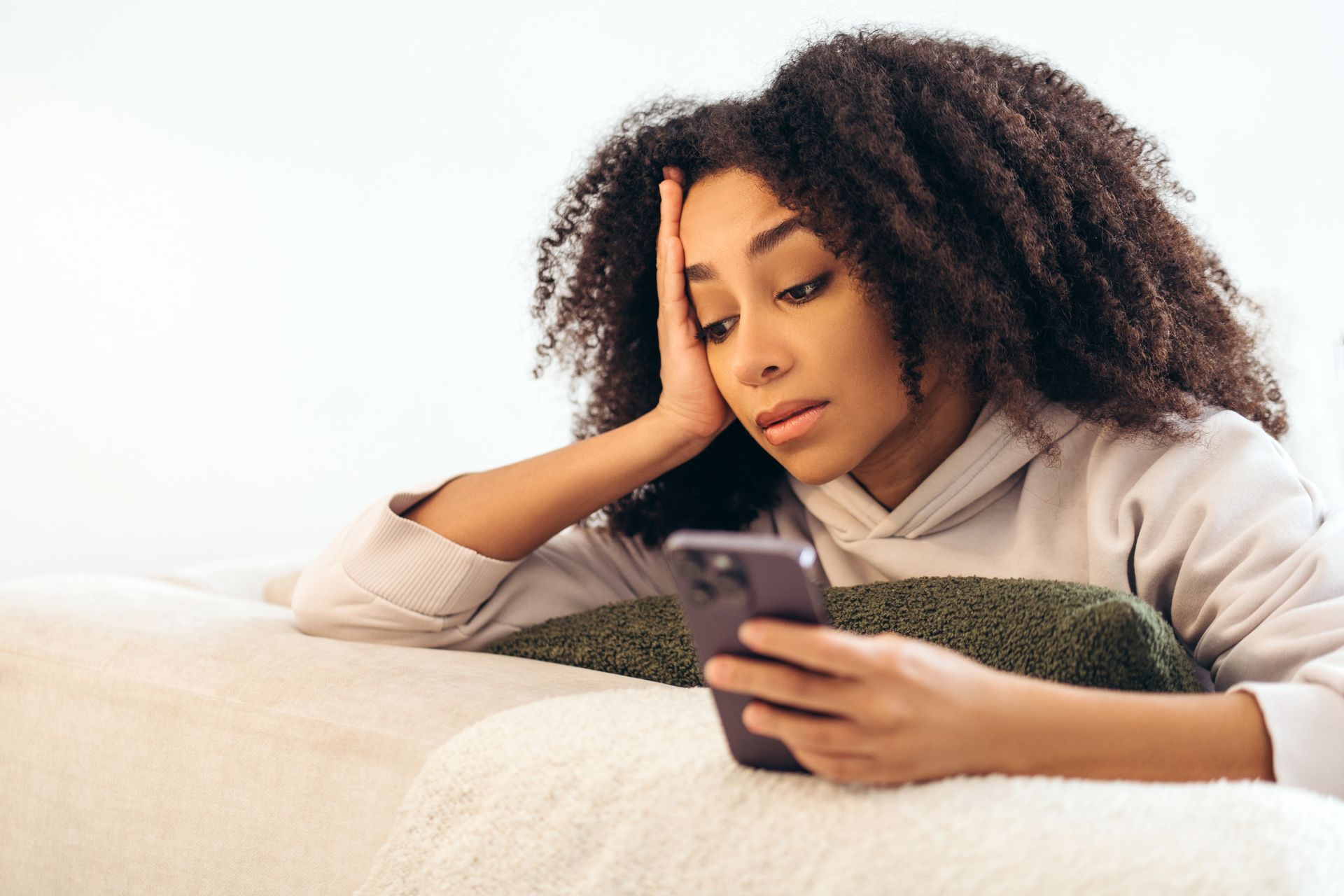 Person lounging on a couch, looking at a smartphone with a thoughtful expression.