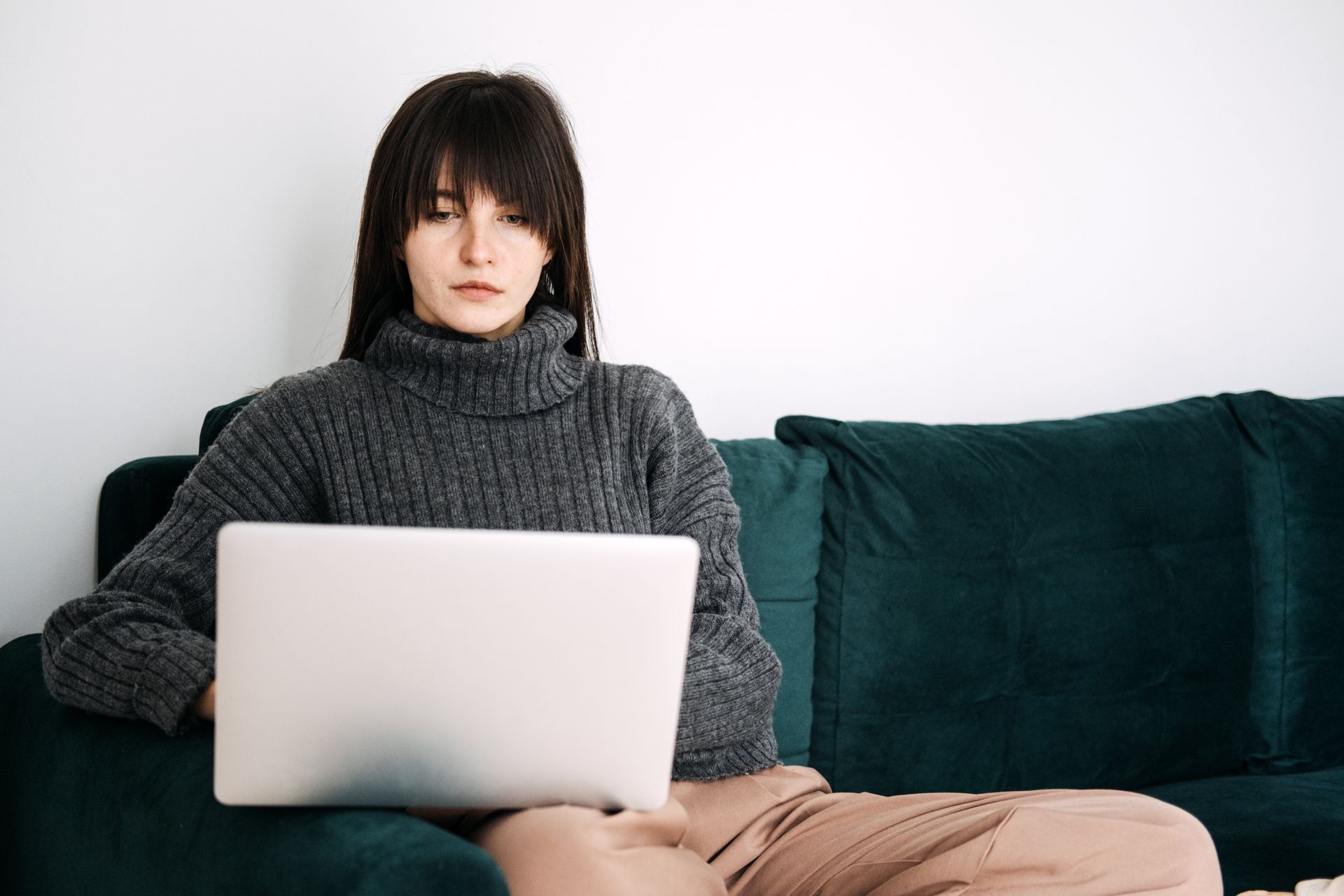 Person in a gray sweater using a laptop while sitting on a teal couch.