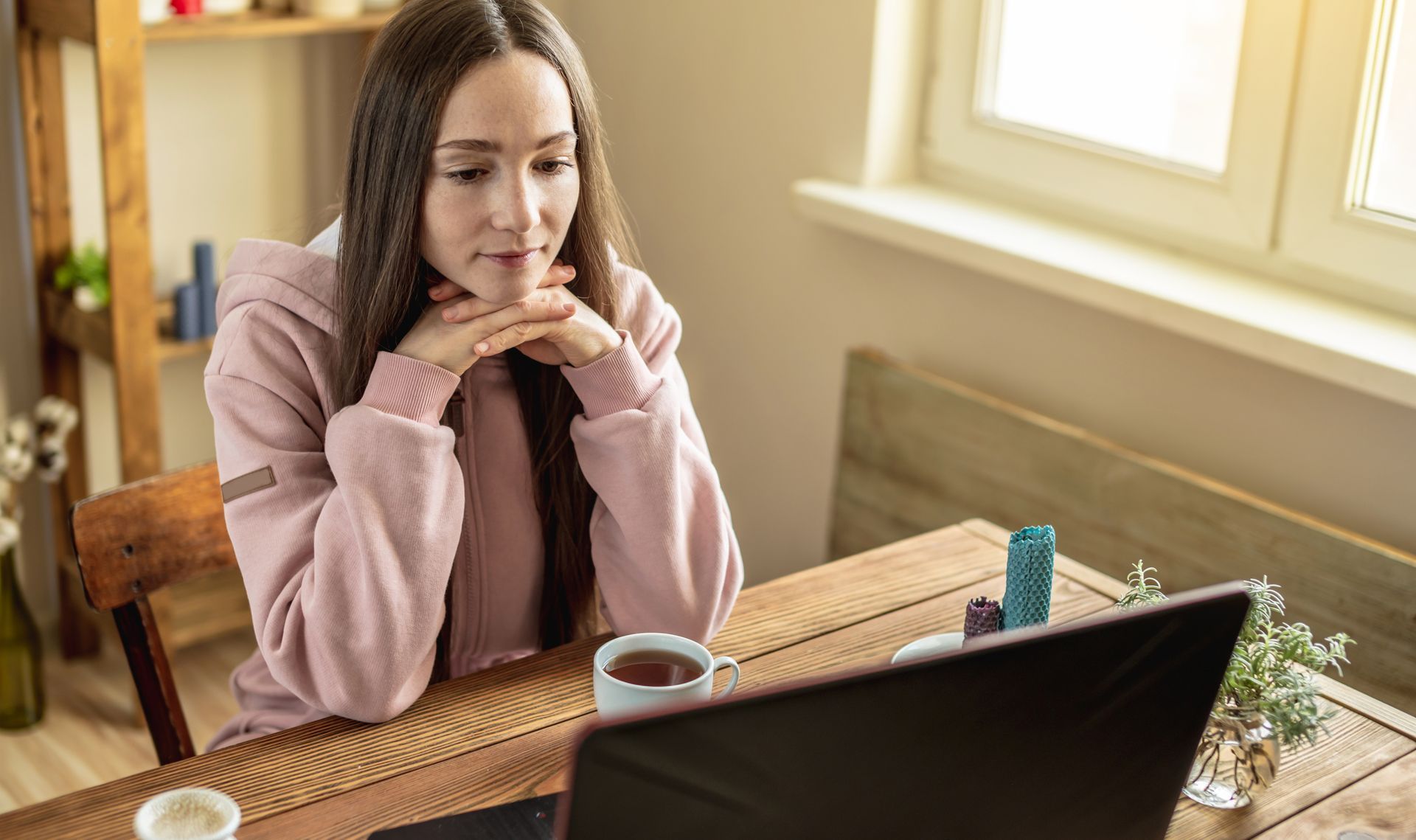 Woman sitting at a desk, looking at a laptop in a bright home office