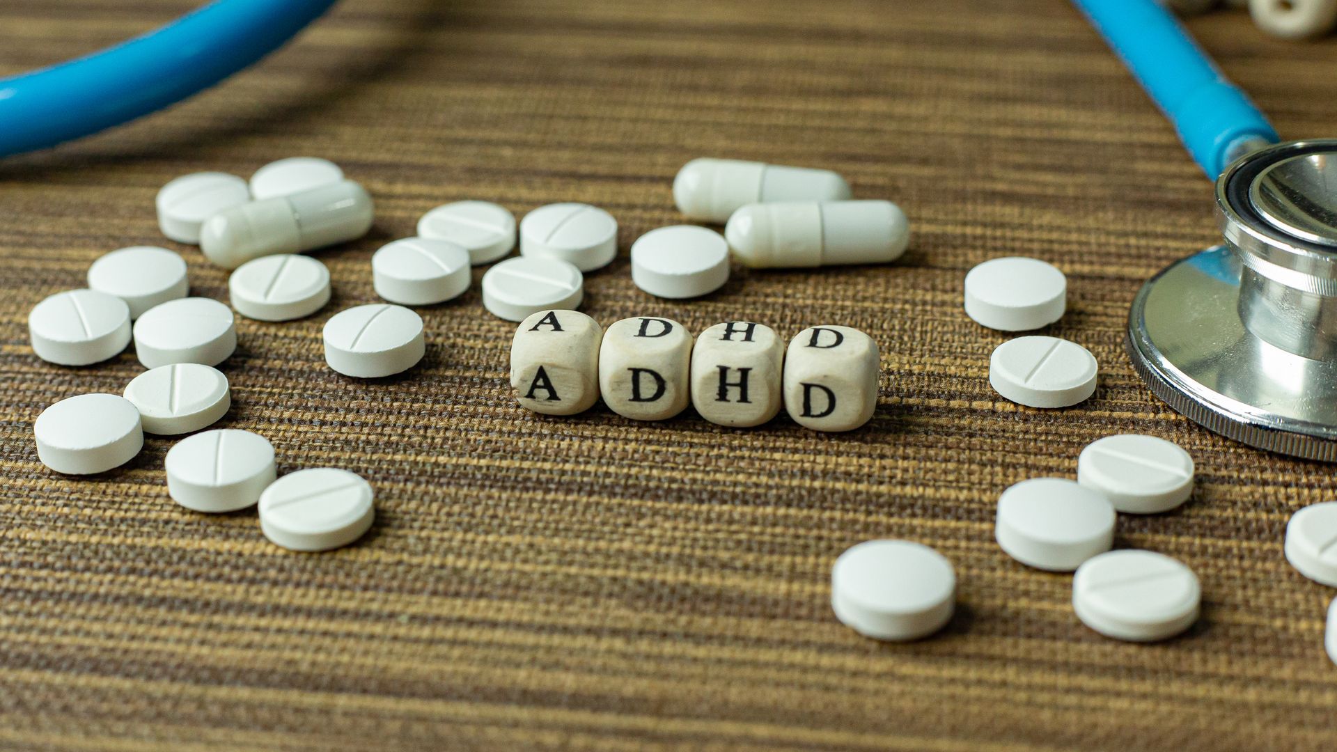 White pills on a table with lettered dice spelling ADHD, beside a stethoscope