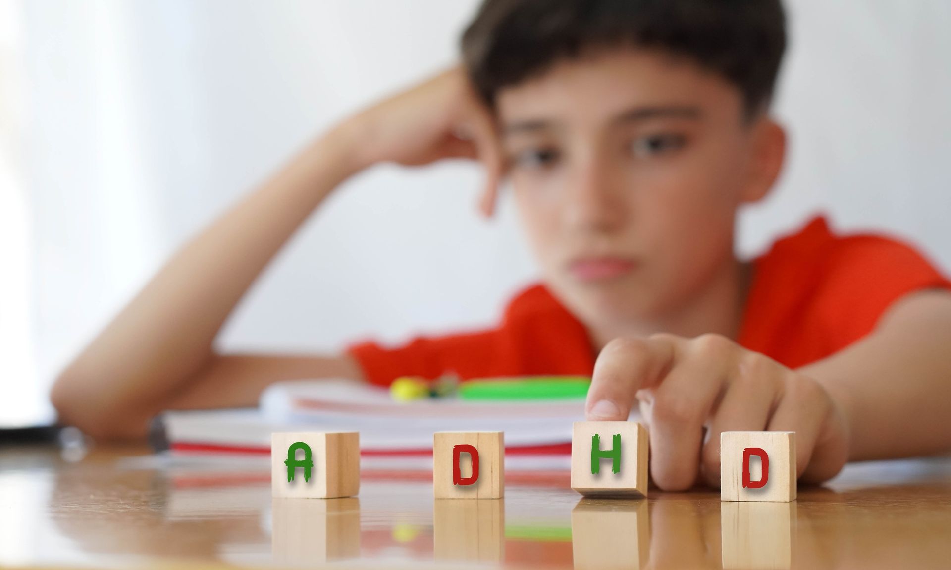 Boy concentrating on letter blocks at a table, with a blurred red toy in the background
