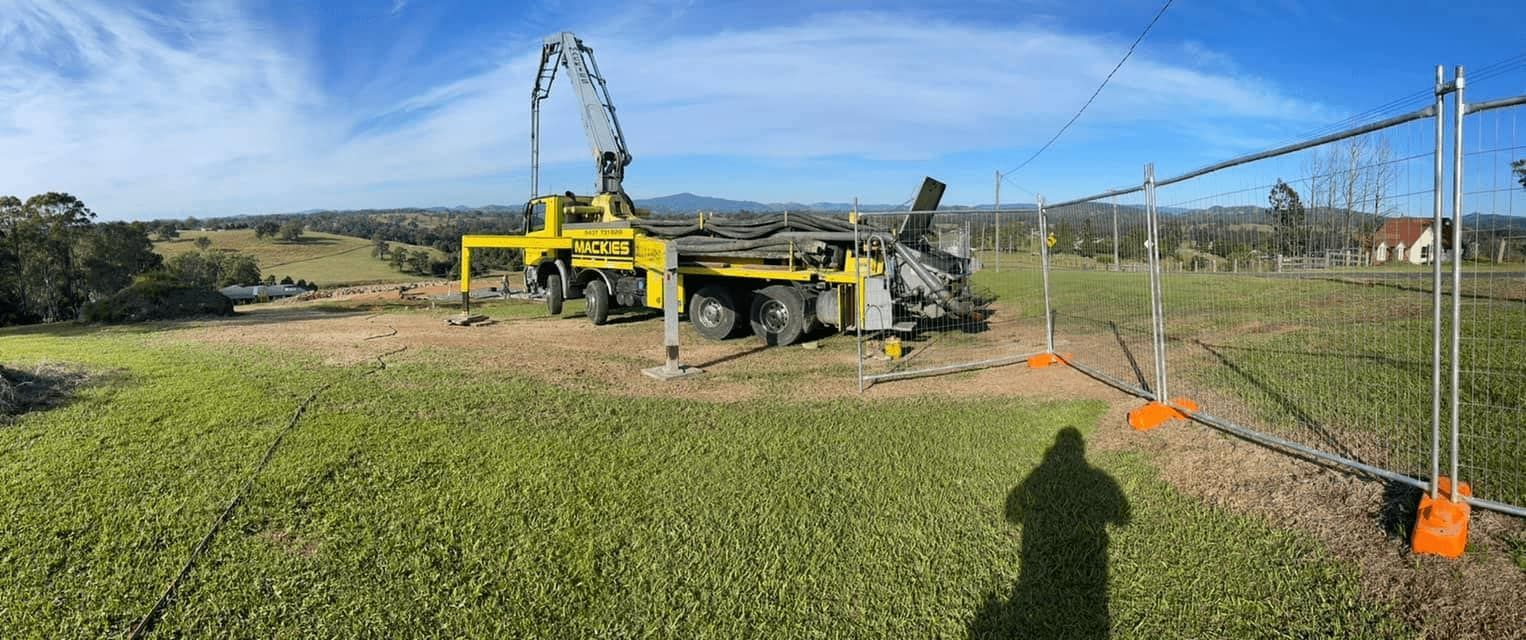 A Large Yellow Truck is Sitting in the Middle of a Grassy Field — Mackie's Concrete Pumping In Gloucester, NSW