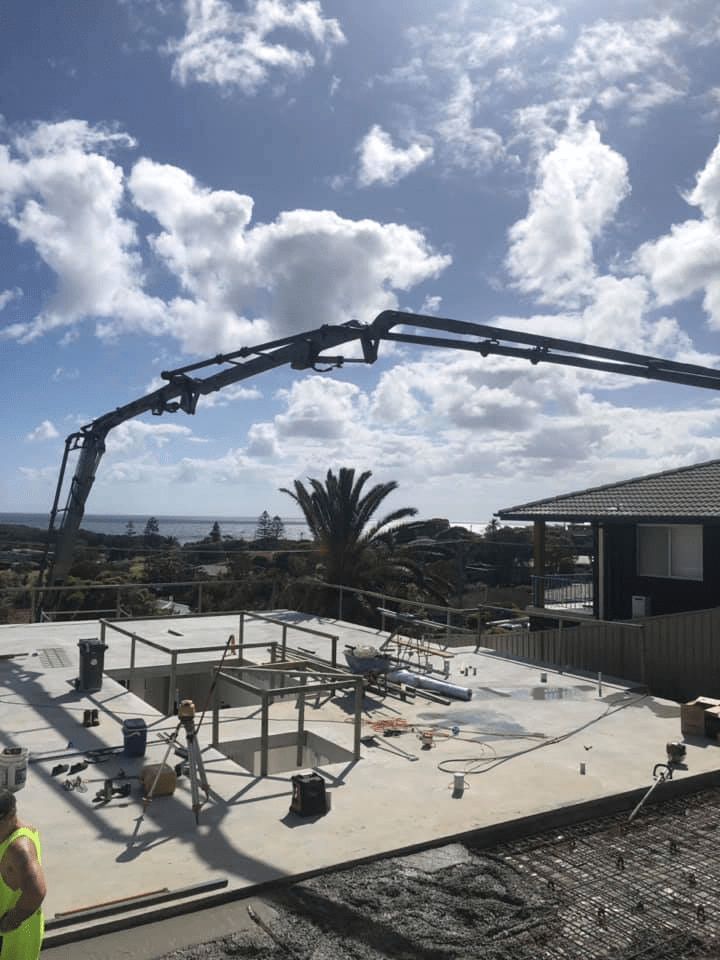 A Man is Standing in Front of a Concrete Pump on a Construction Site — Mackie's Concrete Pumping In Smiths Lake, NSW