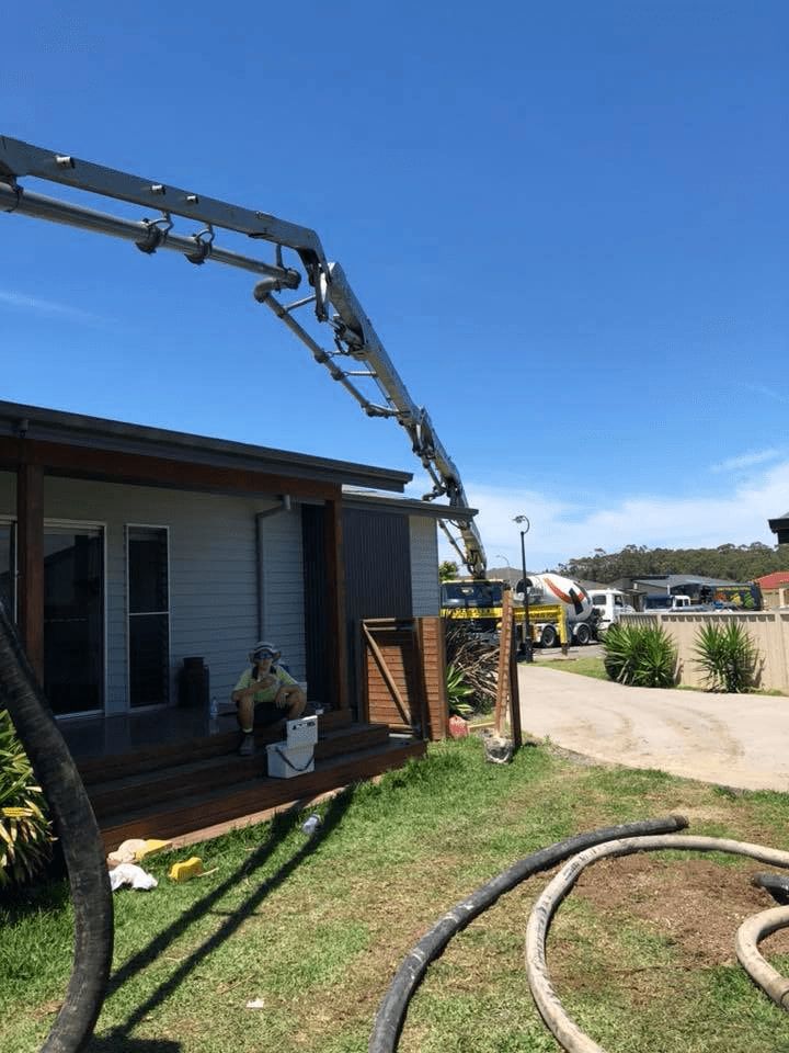 A Man is Sitting on the Porch of a House With a Crane in the Background — Mackie's Concrete Pumping In Old Bar, NSW
