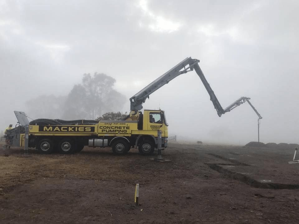 A Yellow Mackie's Truck is Pumping Concrete on a Foggy Day — Mackie's Concrete Pumping In Hallidays Point, NSW