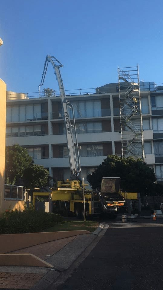 A Large Yellow Crane is Sitting in Front of a Building Under Construction — Mackie's Concrete Pumping In Wingham, NSW