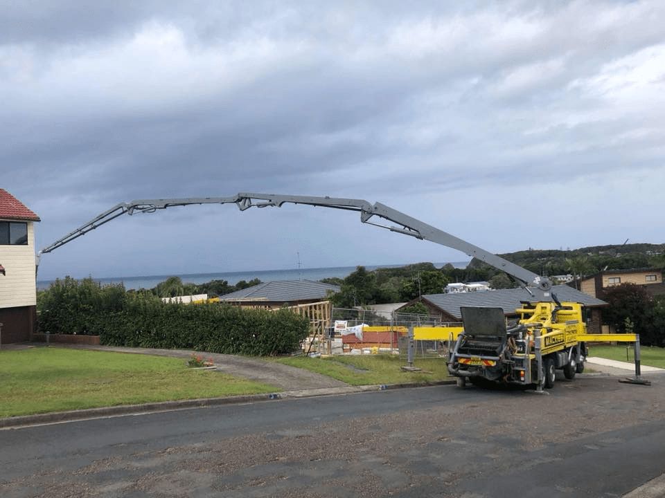 A Concrete Pump Truck is Parked on the Side of the Road in Front of a House — Mackie's Concrete Pumping In Smiths Lake, NSW