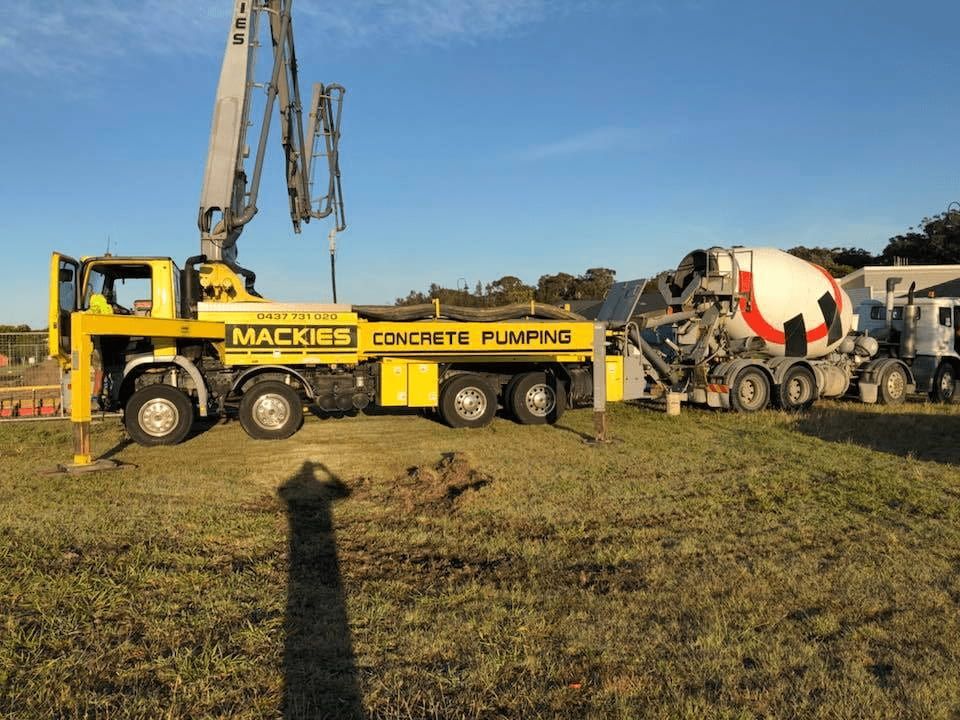 A Concrete Pump Truck is Parked in a Grassy Field Next to a Mixer Truck — Mackie's Concrete Pumping In Harrington, NSW