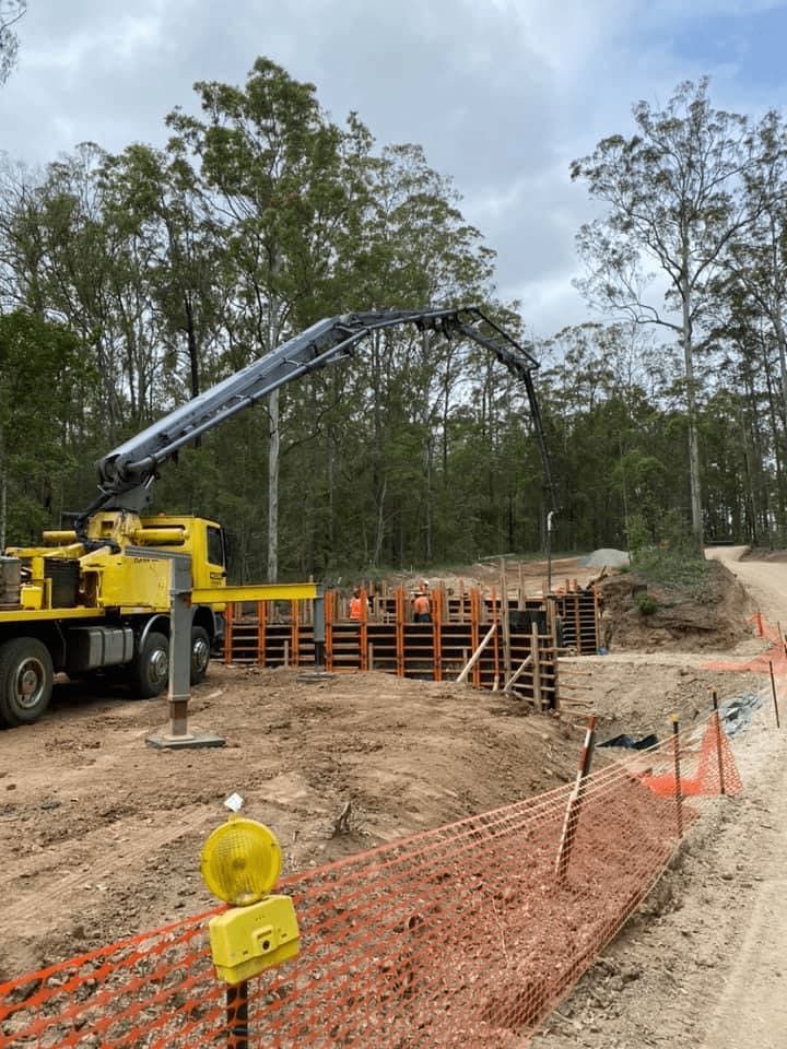A Yellow Truck is Driving Down a Dirt Road Next to a Construction Site — Mackie's Concrete Pumping In Gloucester, NSW