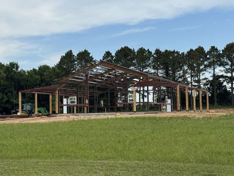 Partially built wooden house frame in a grassy field with trees in the background