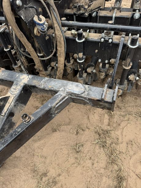 Close-up of a muddy tractor hitch and hydraulic components on a dirt surface.