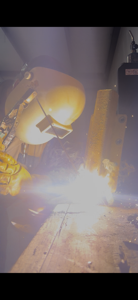 Bright welding scene with sparks and a large industrial machine in a dim workshop