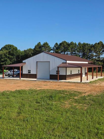Rural metal barn with open-sided sheds on a dirt lot under a clear blue sky