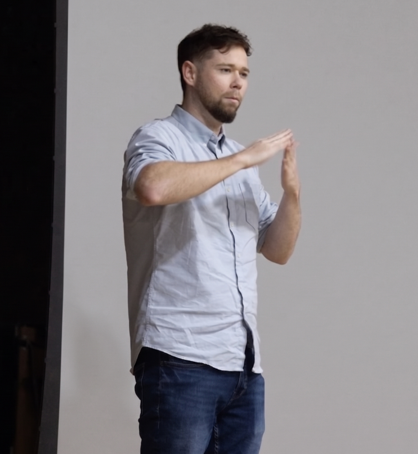 Man gesturing with raised hands against a plain gray background