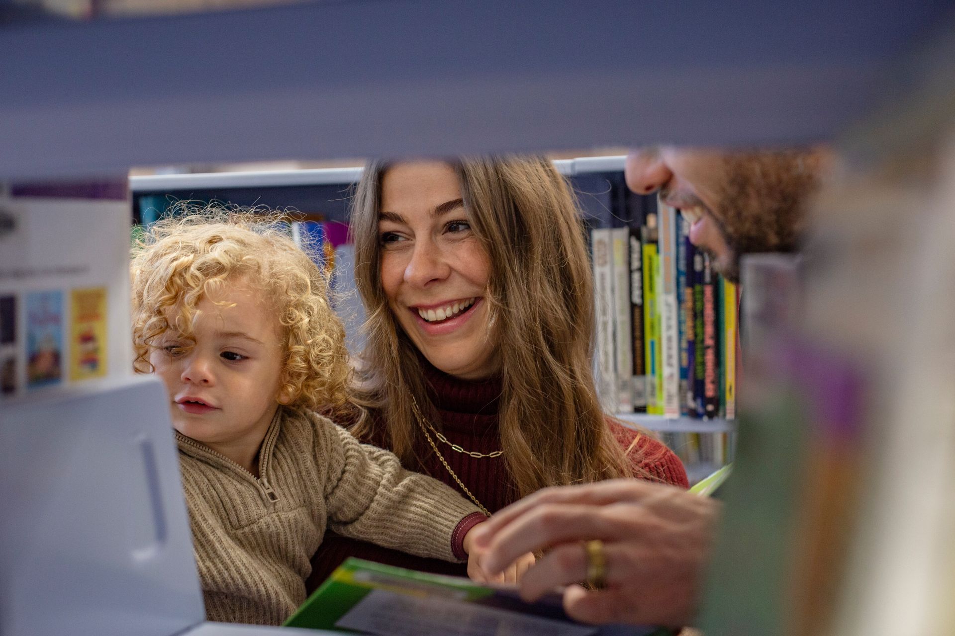 Child and smiling adult at a library computer, with bookshelves in the background