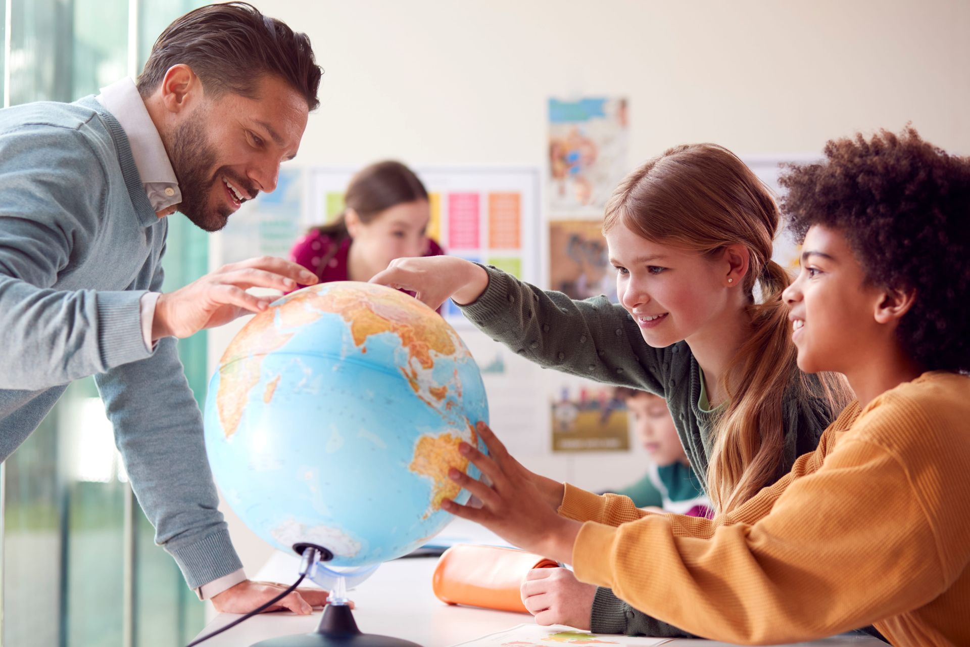 Students and teacher gathered around a globe in a classroom, pointing and smiling.