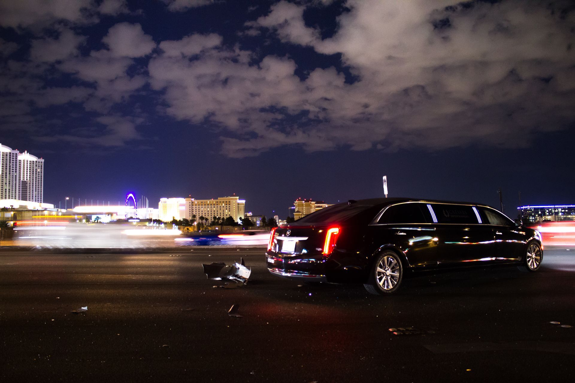 Black luxury car driving at night on a city street with blurred lights and cloudy sky Black luxury car driving at night on a city street with blurred lights and cloudy sky