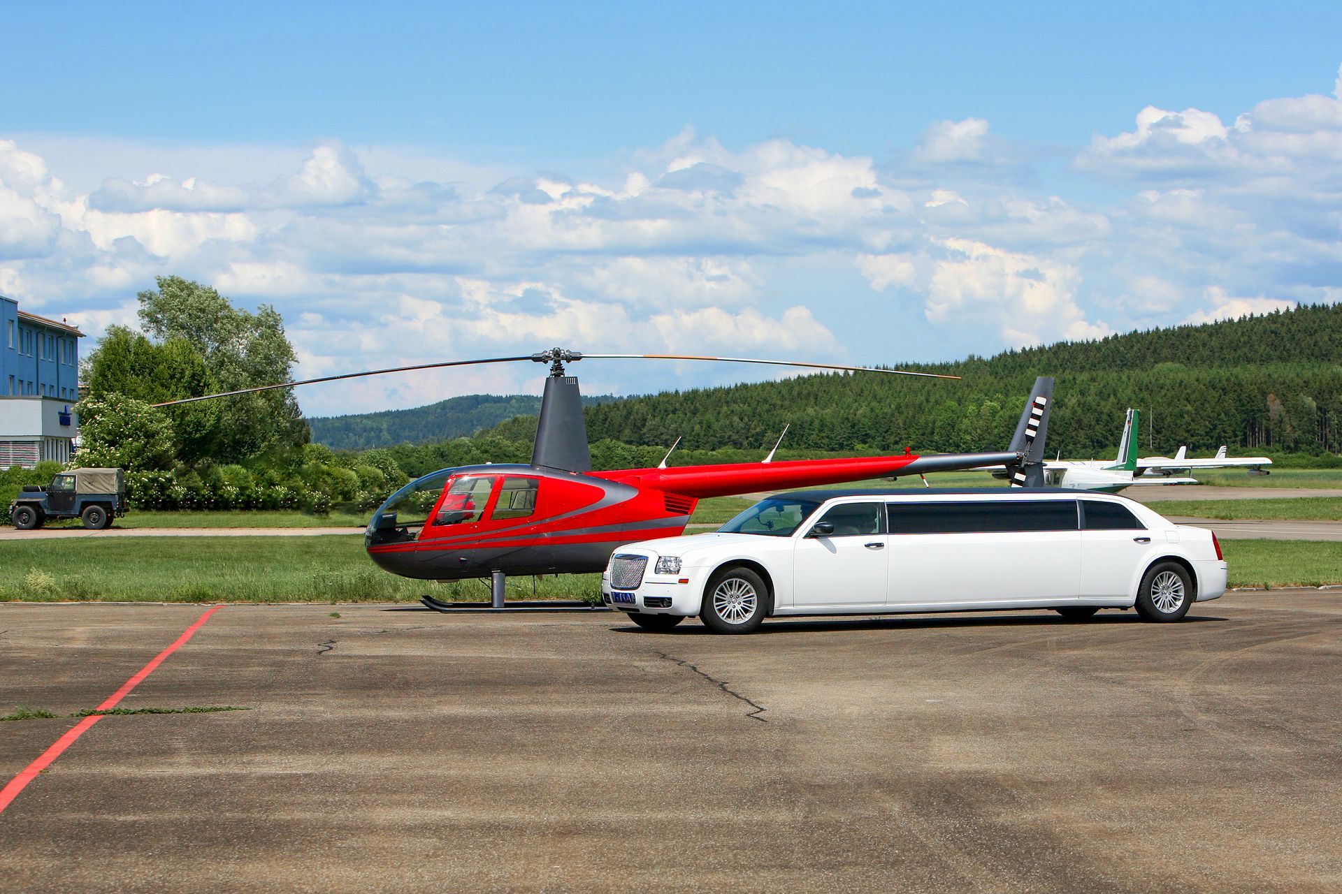 Red helicopter and white stretch limousine on a runway under a blue, cloudy sky Red helicopter and white stretch limousine on a runway under a blue, cloudy sky