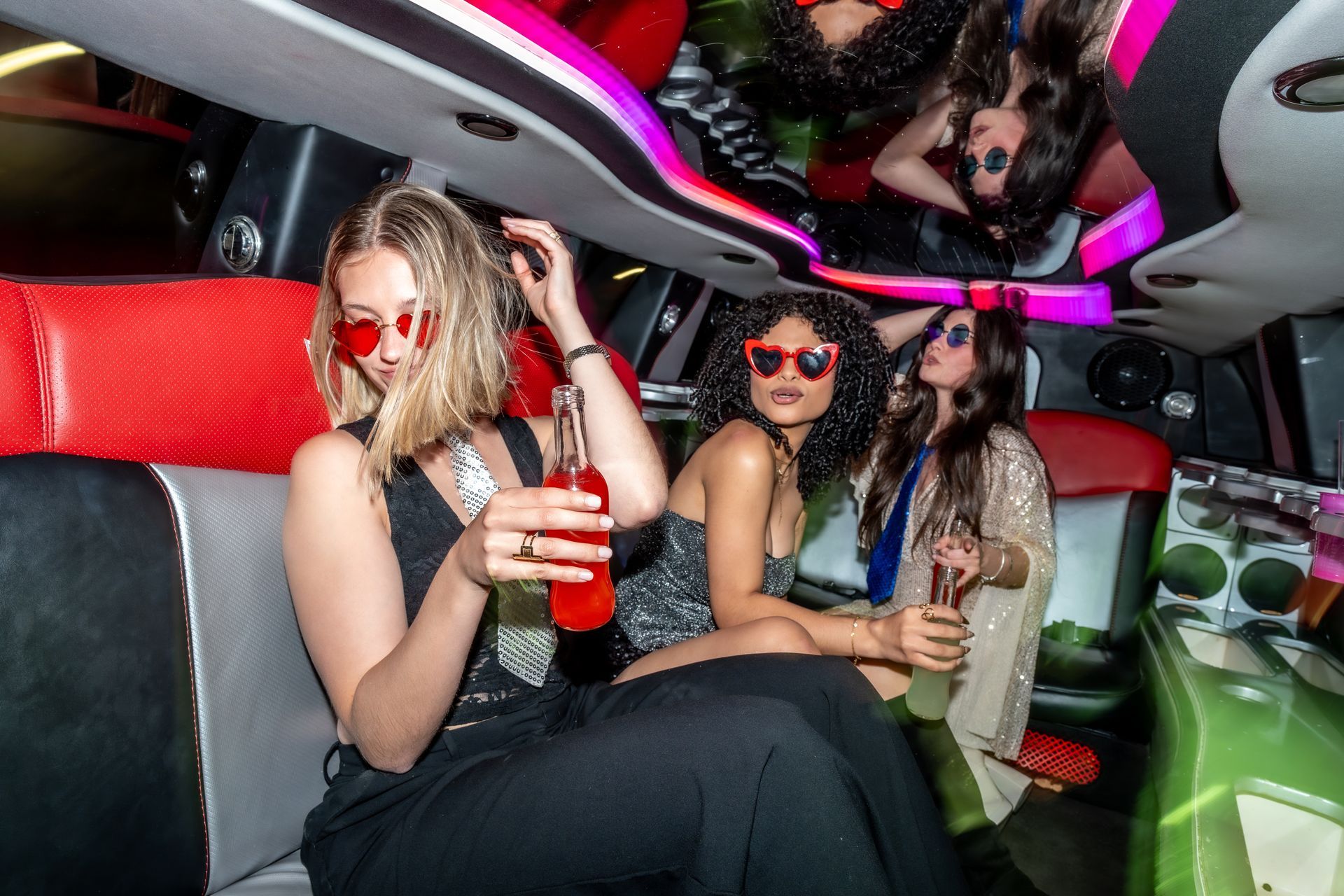 Two women wearing sunglasses in a neon-lit limousine, holding drinks and smiling Two women wearing sunglasses in a neon-lit limousine, holding drinks and smiling
