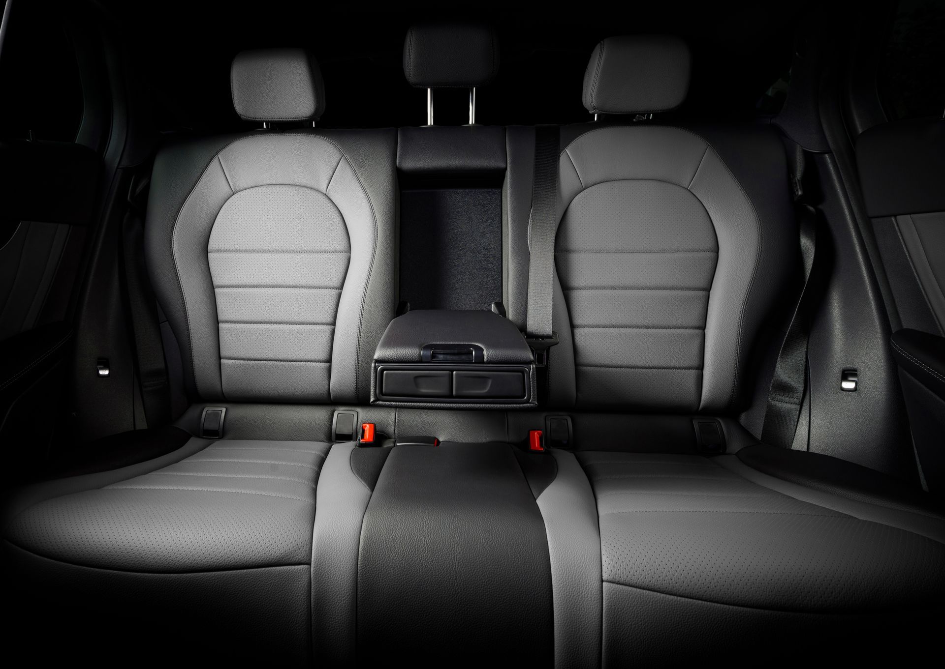 Car interior rear seat with black and gray upholstery, center armrest, and red seatbelt buckles. Car interior rear seat with black and gray upholstery, center armrest, and red seatbelt buckles.